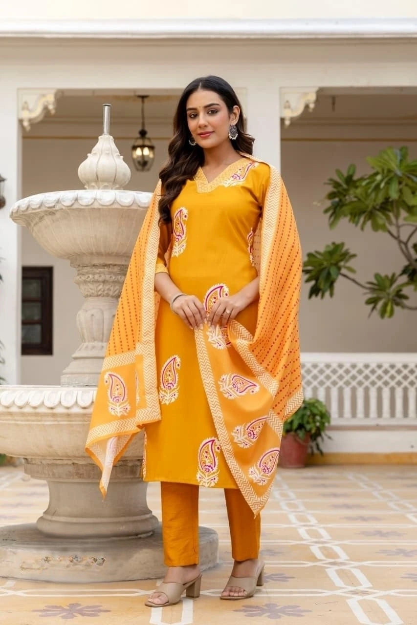Woman in a yellow traditional outfit with a dupatta standing in front of a decorative fountain.