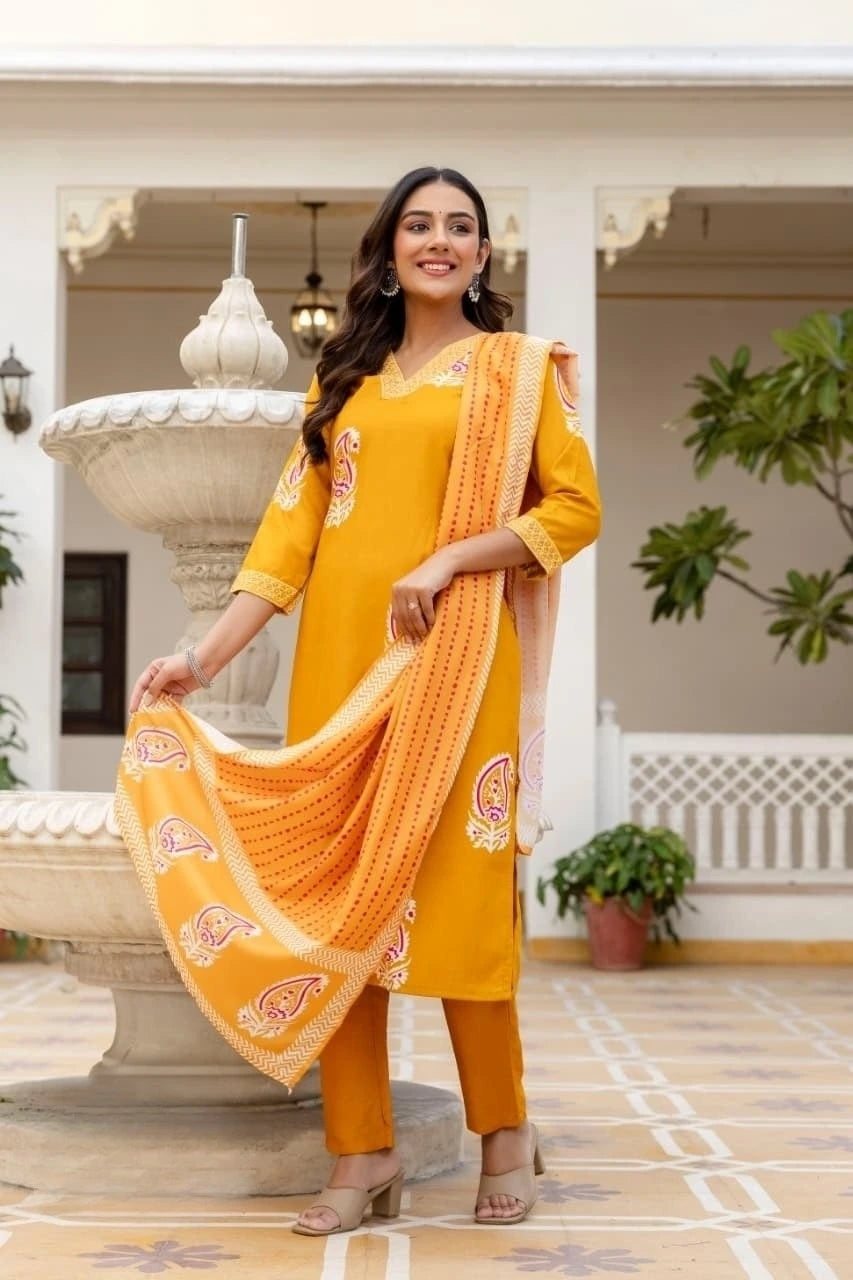 Woman in a yellow traditional outfit with an orange dupatta standing in front of a decorative fountain.