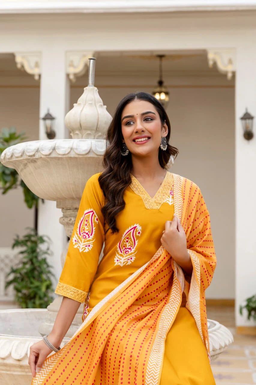 Woman in a yellow and orange traditional outfit standing in front of an architectural structure.
