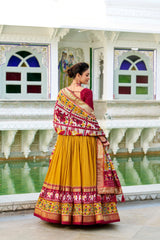 Woman in a traditional yellow and multicolored saree standing in front of a decorative wall with stained glass windows.