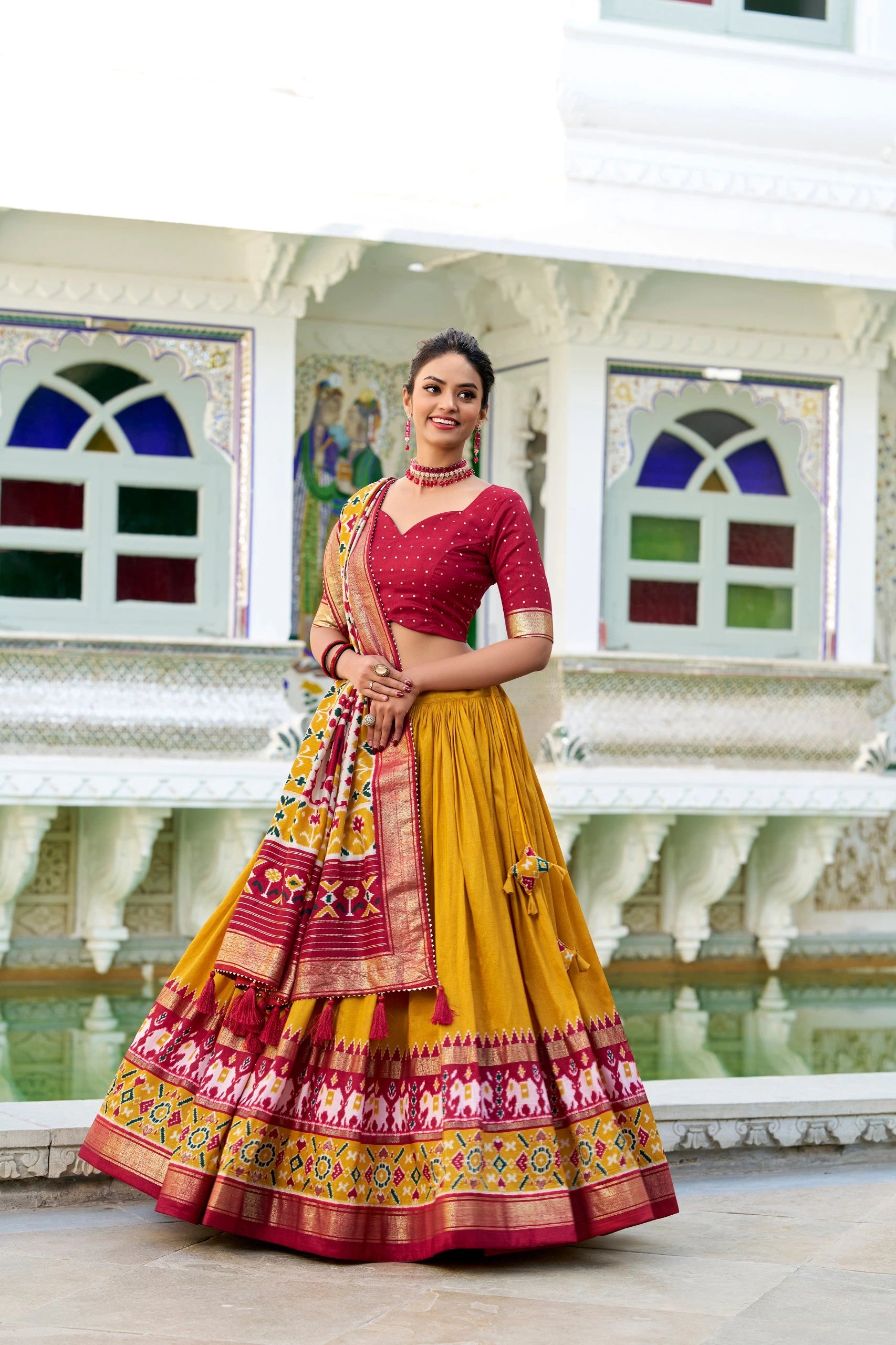 Woman in a colorful traditional outfit standing in front of a decorative wall.
