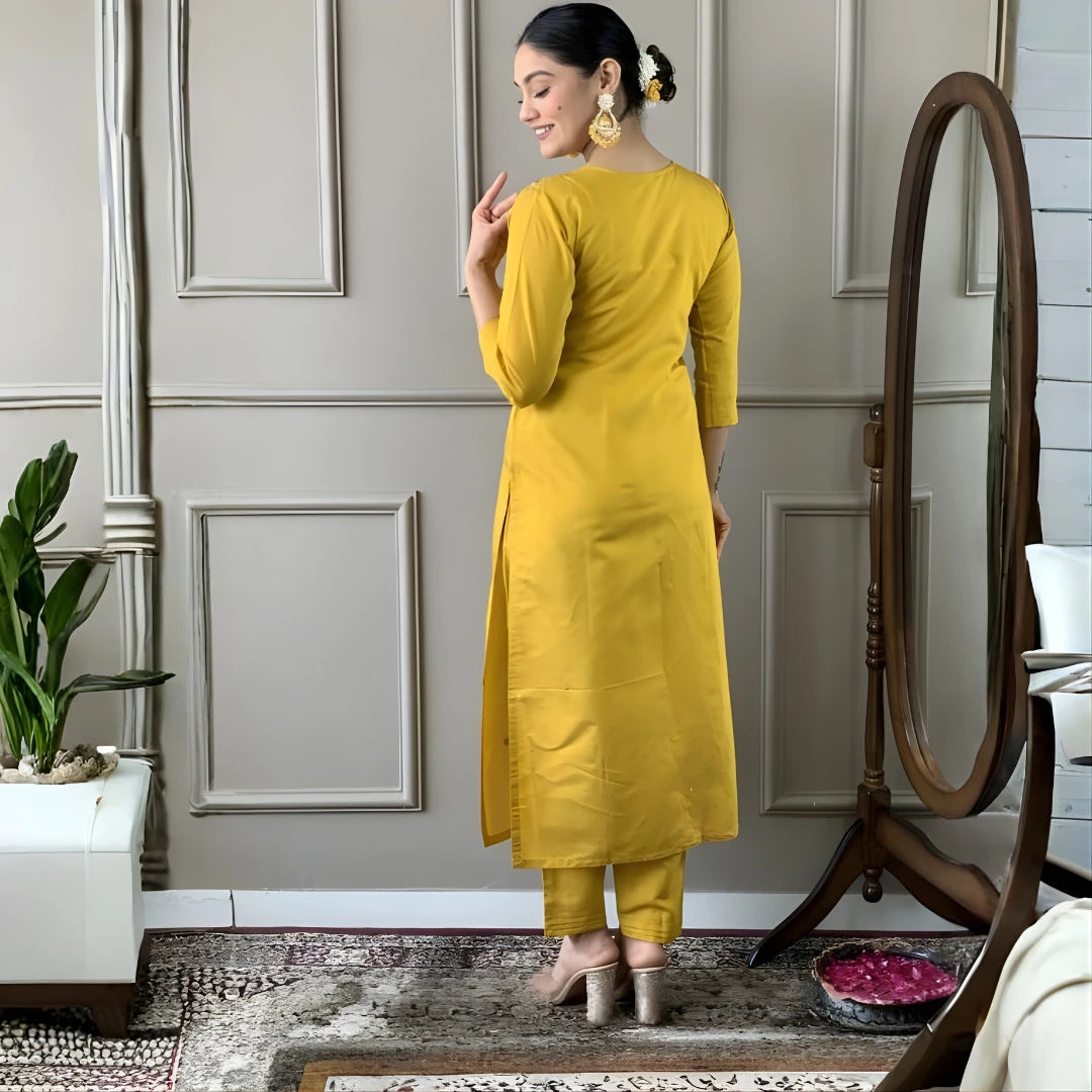 Woman in a yellow outfit standing in a room with a mirror and plant.
