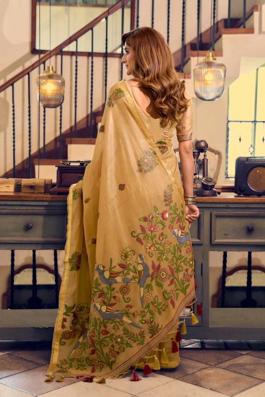 Woman in a yellow saree with floral patterns in a room with wooden staircase and vintage decor.