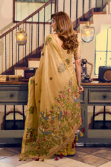 Woman in a yellow saree with floral patterns in a room with wooden staircase and vintage decor.