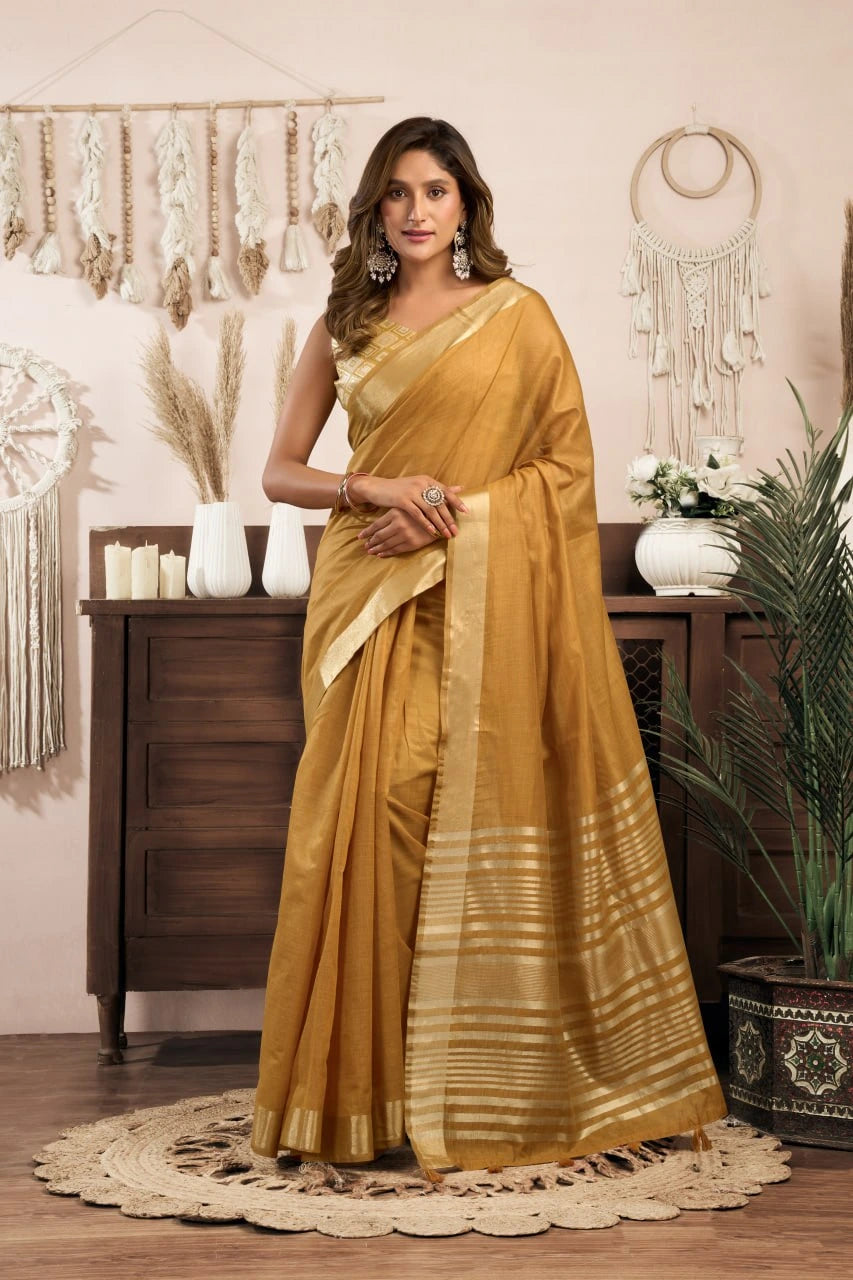 Woman in a mustard yellow saree standing in a decorated room with plants and decor.