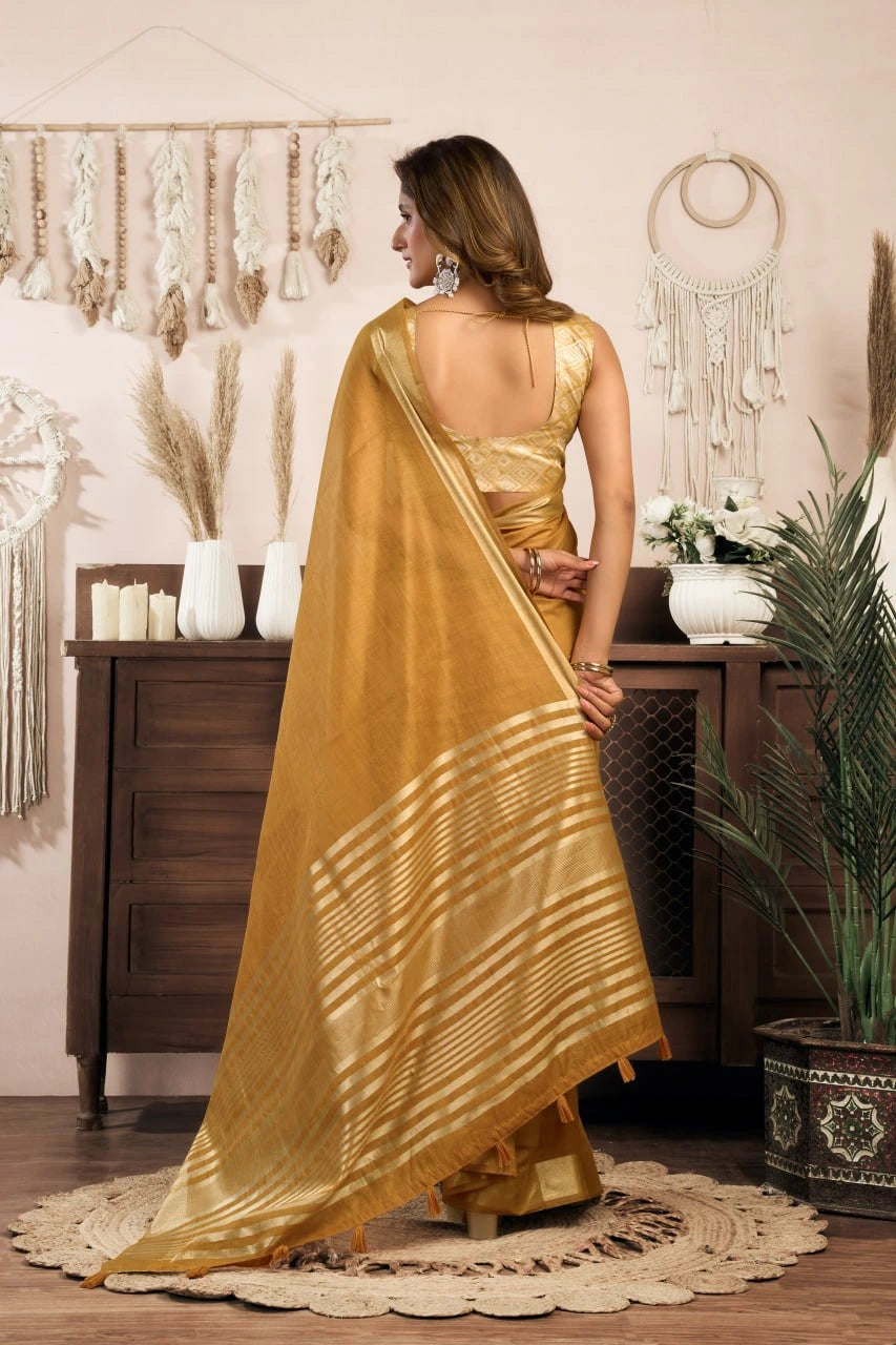 Woman in a gold saree standing in a room with decorative elements.