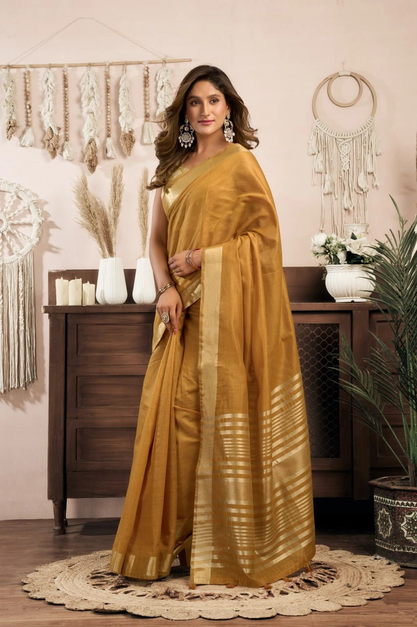 Woman in a mustard yellow saree standing in a room with decorative elements.