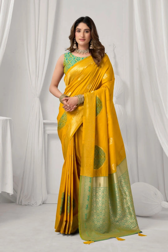 Woman wearing a yellow saree with green patterns against a white curtain background