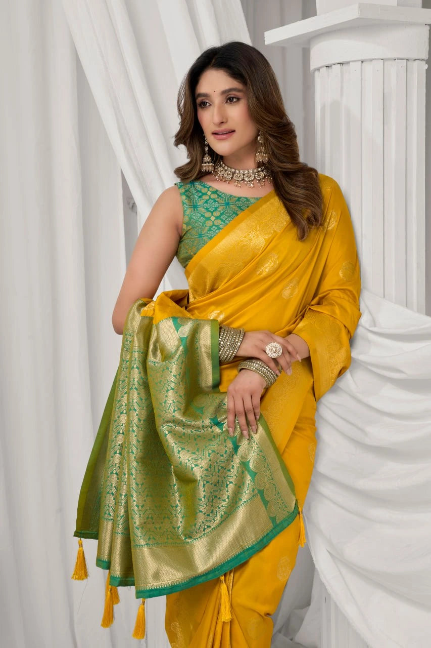 Woman wearing a yellow saree with green blouse against a white curtain background
