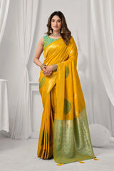 Woman wearing a yellow saree with green patterns against a white curtain background