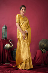 Woman in a gold saree standing against a red background with decorative items.