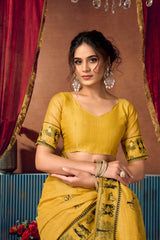 Woman wearing a yellow saree with black patterns against a decorative curtain background