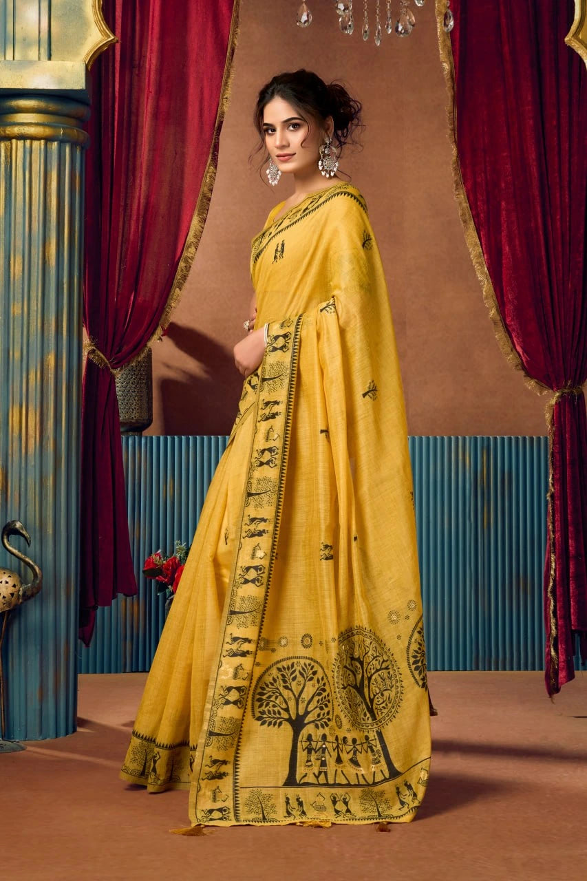 Woman in a yellow saree with black patterns standing in front of red curtains.