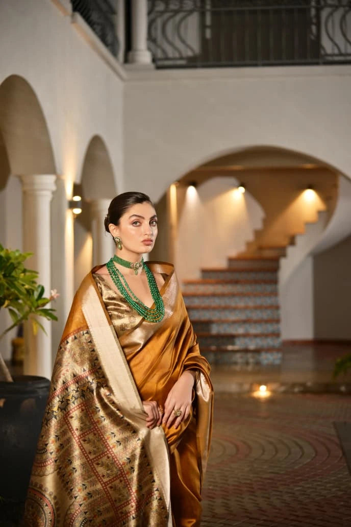 Woman in a gold saree with intricate patterns in an elegant interior setting.