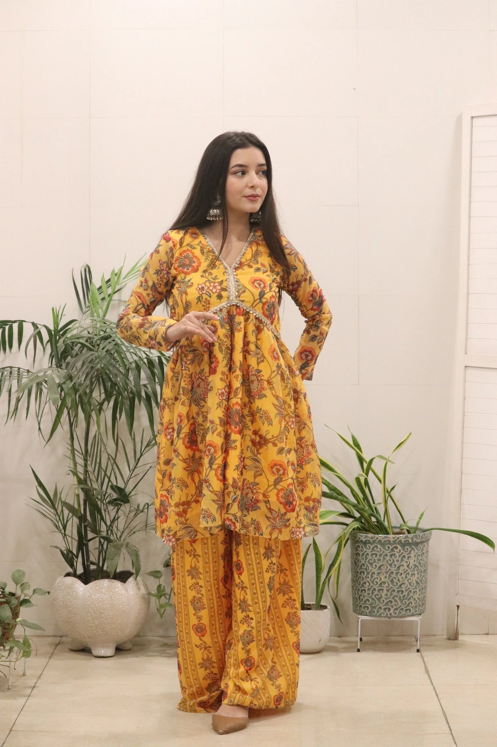 Woman in a yellow floral outfit standing in a room with plants.