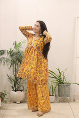 Woman in a yellow floral outfit standing indoors with plants in the background