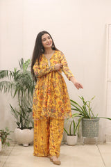 Woman wearing a yellow floral outfit standing indoors with plants in the background