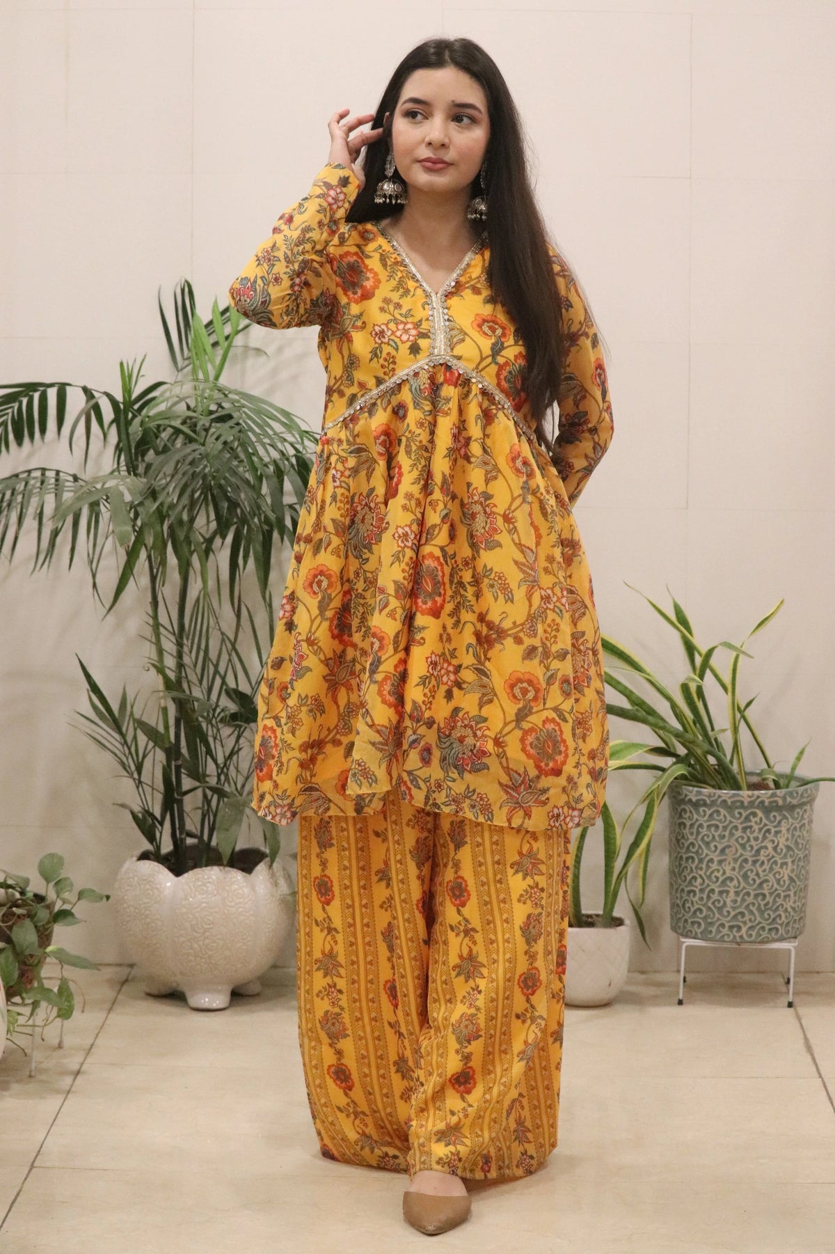 Woman wearing a yellow floral outfit standing in a room with plants.