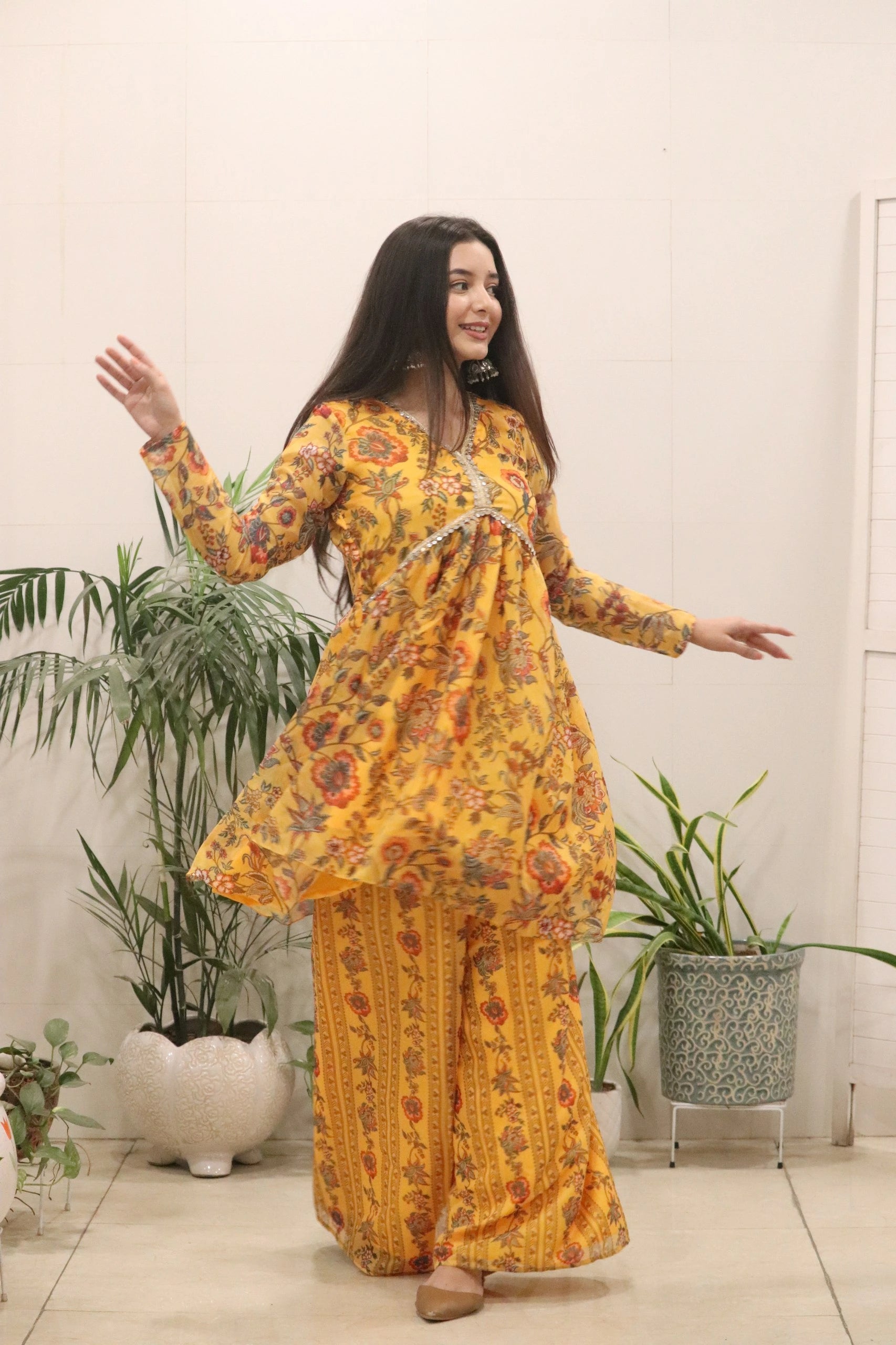Woman in a yellow floral dress standing indoors with plants in the background