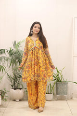 Woman wearing a yellow floral outfit standing in a room with plants.