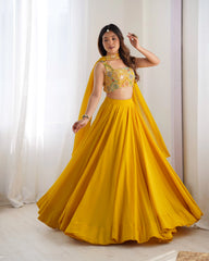 Woman wearing a yellow traditional outfit with a floral top and flowing skirt against a white curtain background.