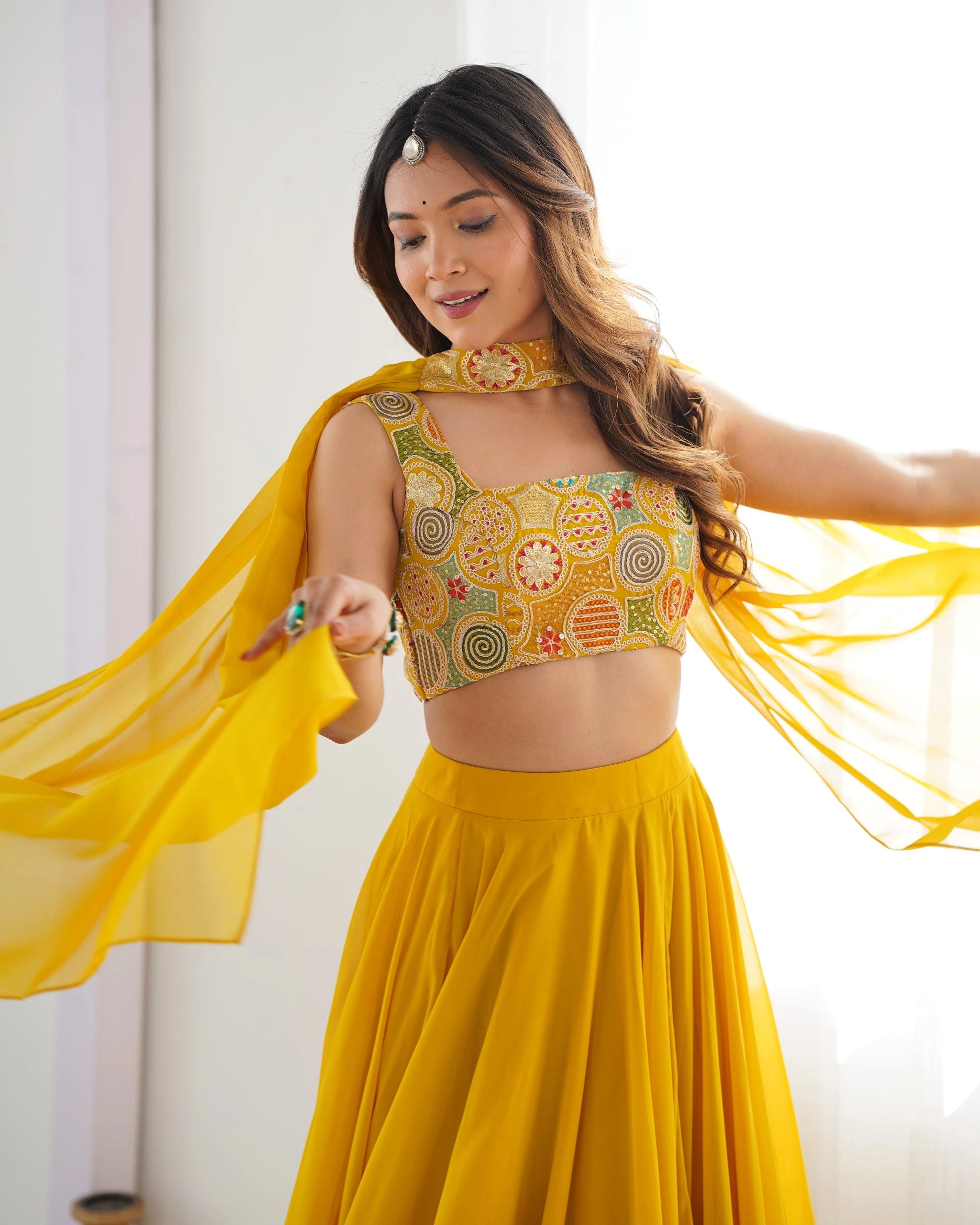 Woman in a yellow traditional outfit with a patterned top and flowing fabric against a white background