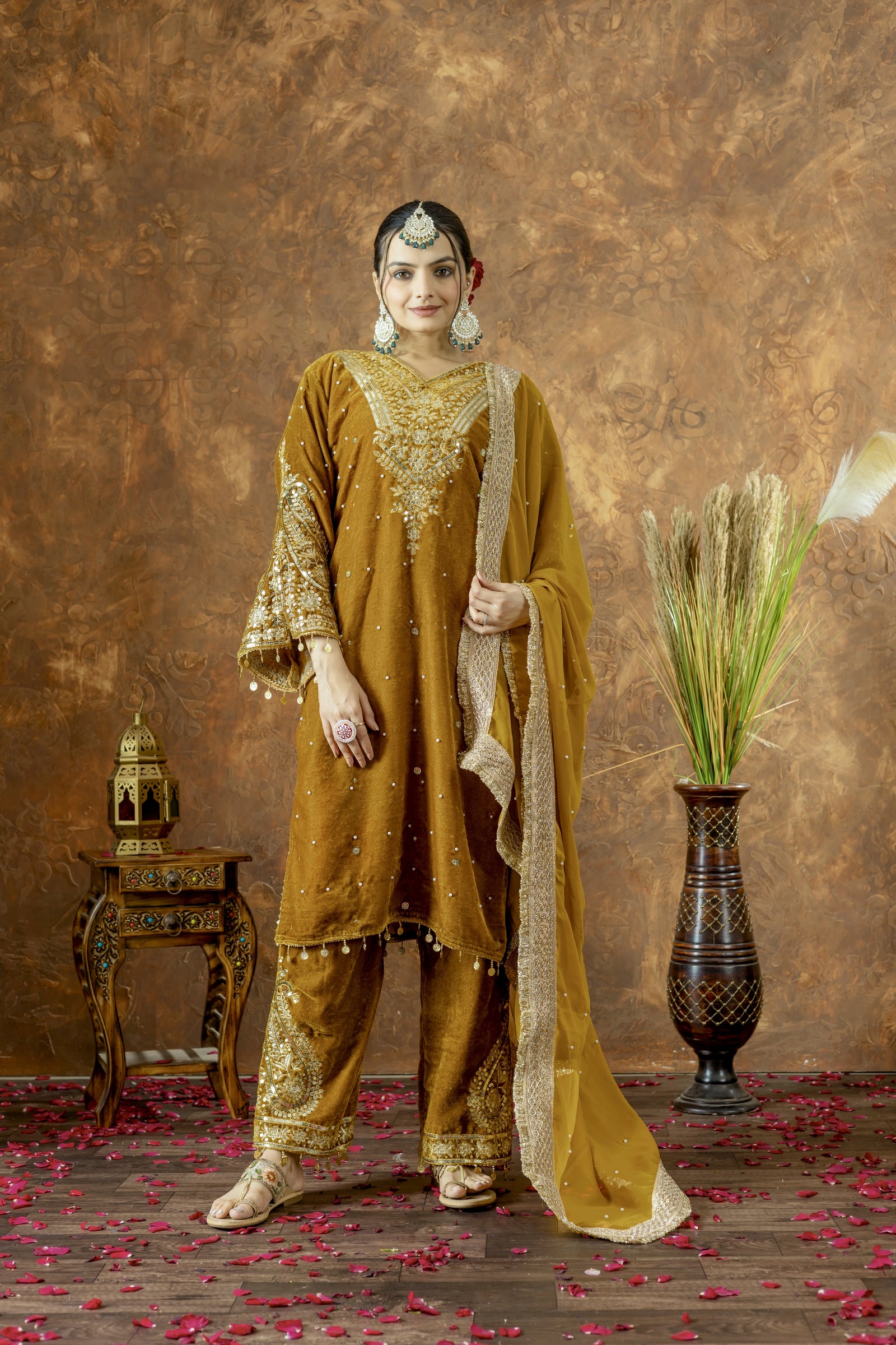 Woman in traditional mustard yellow outfit with gold embroidery against a textured brown background