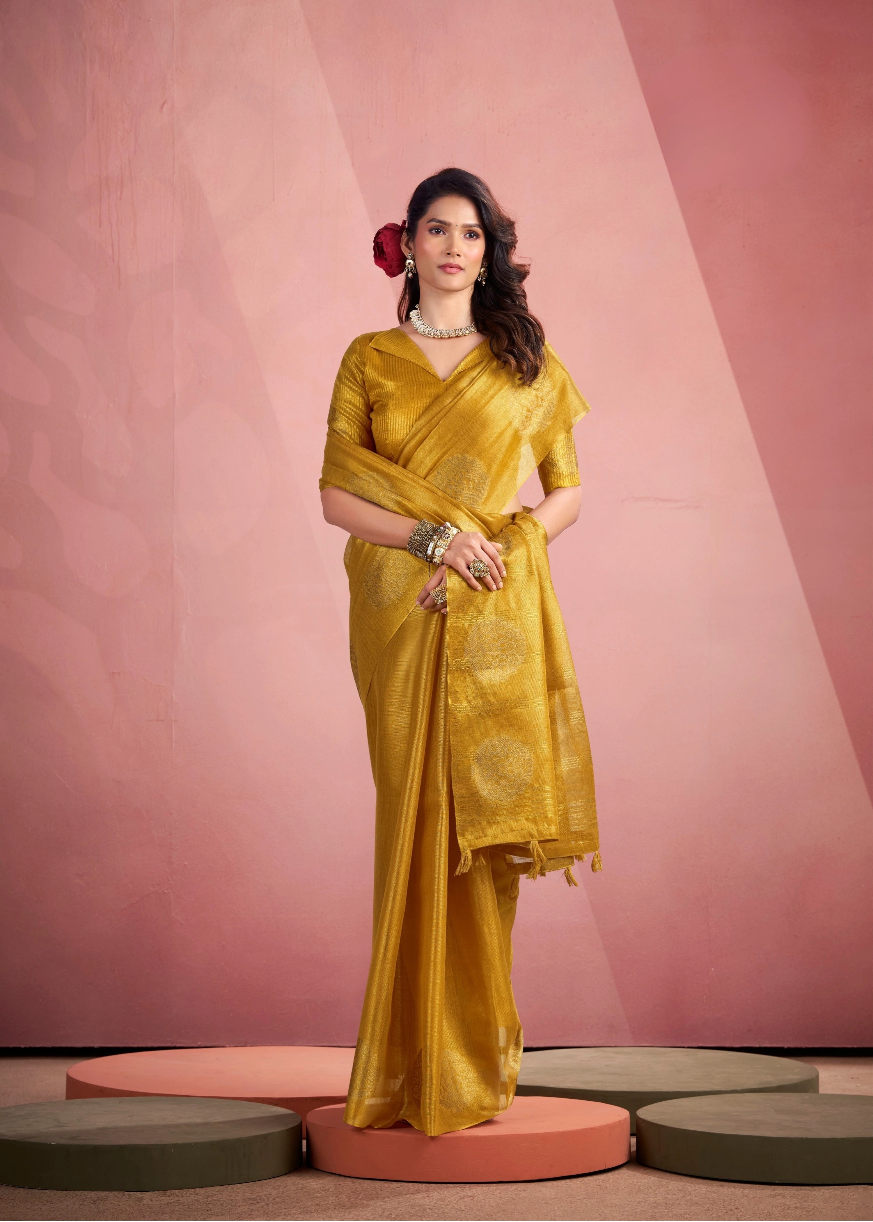 Woman in a yellow saree standing on a pink platform with a pink background