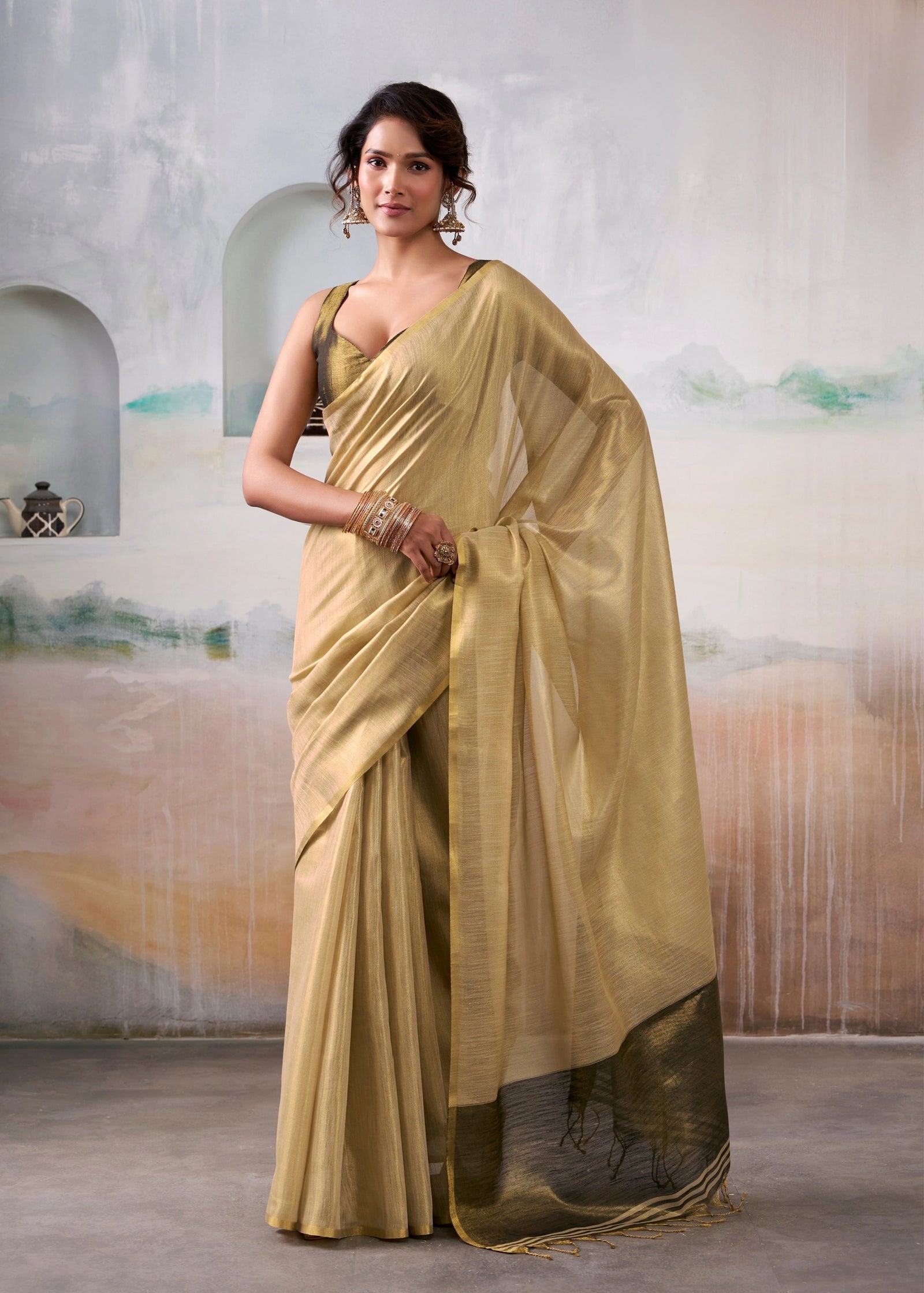Woman wearing a gold saree with a textured wall background