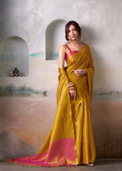 Woman wearing a yellow saree with pink blouse against a textured wall.