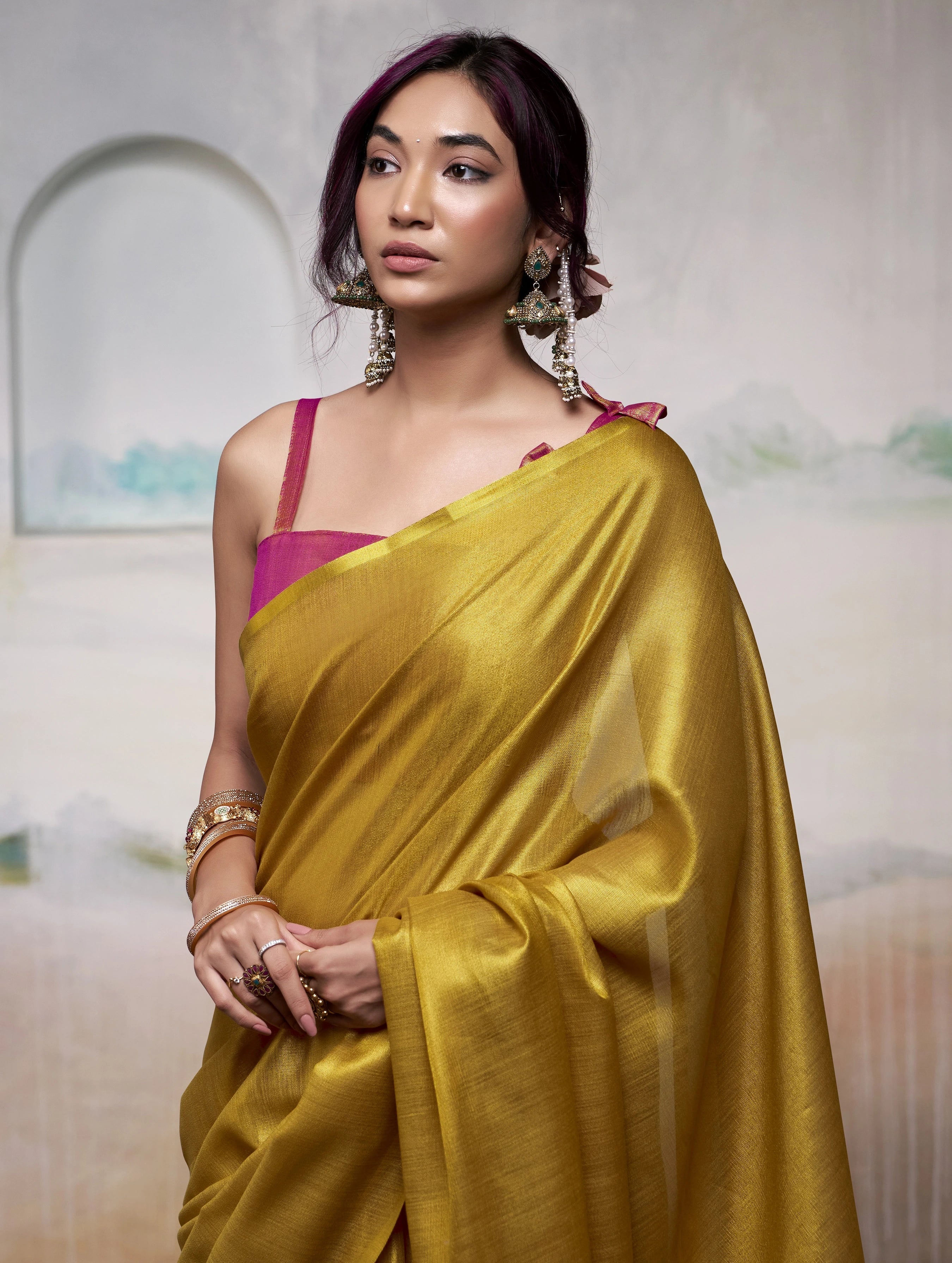 Woman wearing a yellow saree with a pink blouse against a blurred background