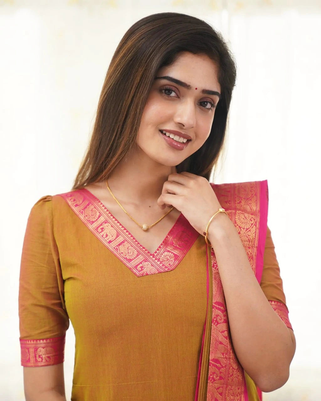 Woman wearing a mustard yellow saree with pink border on a white background