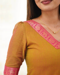 Woman wearing a mustard yellow top with pink embroidery on a white background