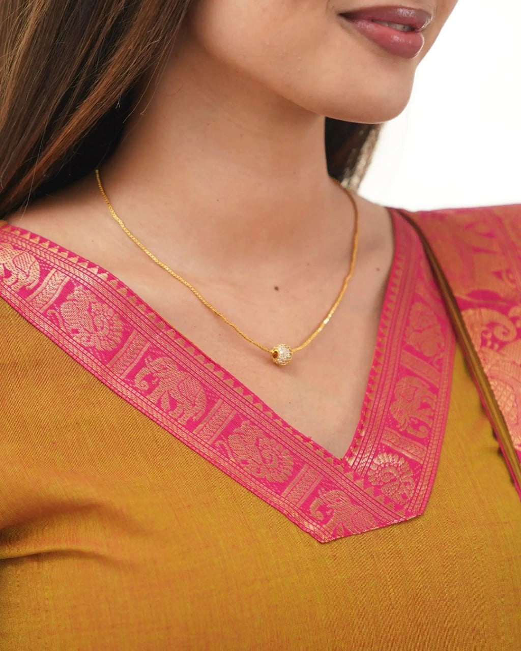 Close-up of a person wearing a gold necklace with a pink blouse