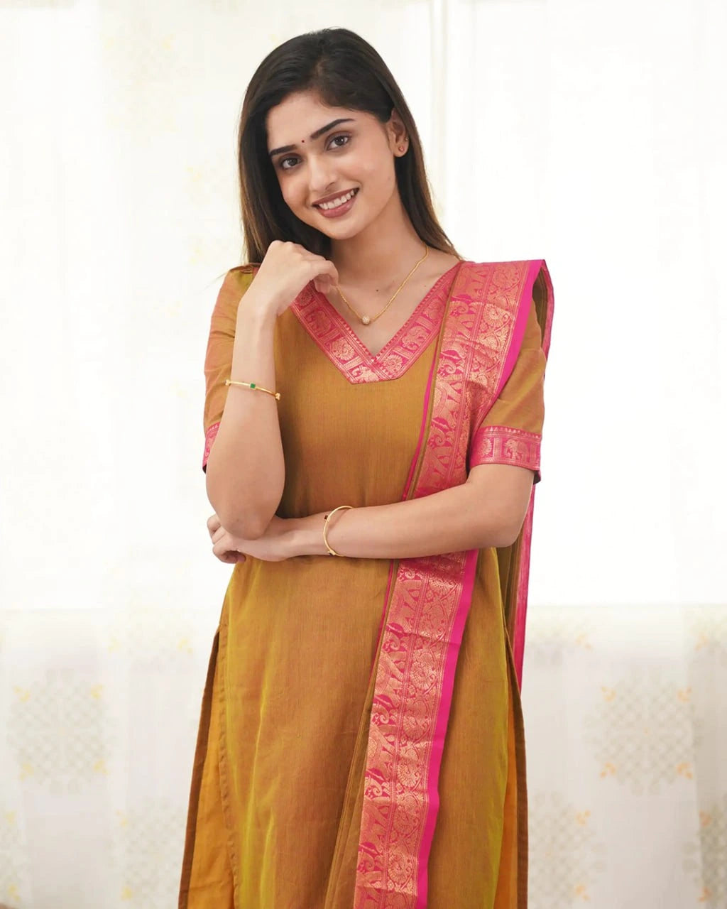 Woman wearing a mustard yellow saree with pink border on a white background