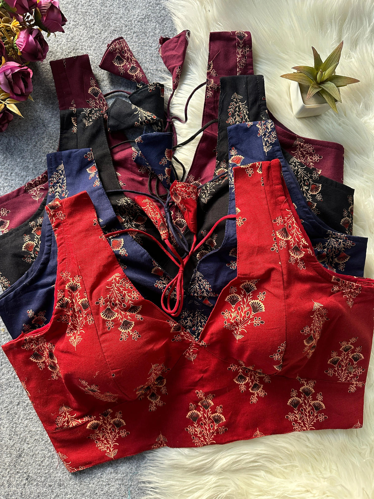 Red floral lingerie set on a textured surface with flowers and a plant in the background