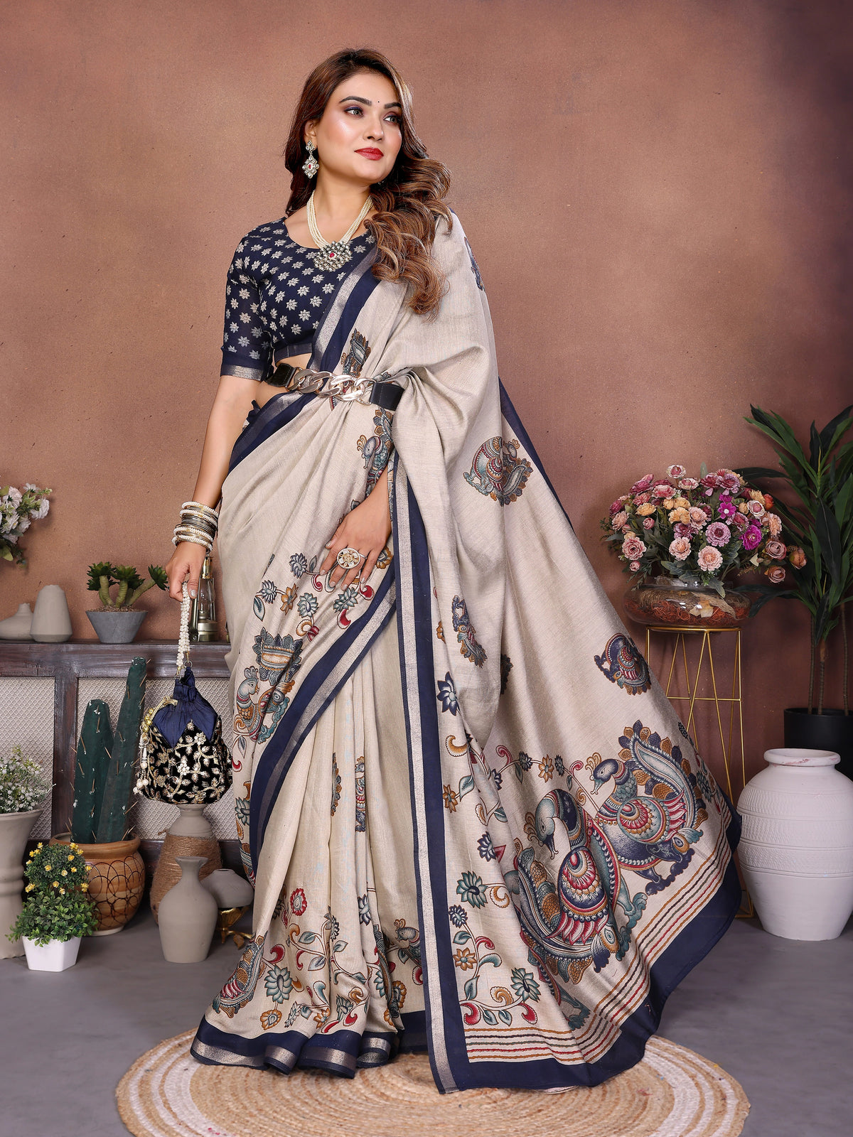 Woman wearing a traditional saree with intricate patterns in a decorated indoor setting.