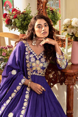 Woman in a blue embroidered traditional outfit sitting in a decorated room with flowers and a mirror.