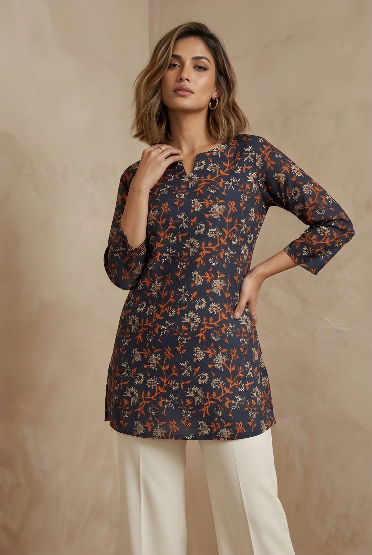 Woman wearing a patterned navy blue top with white pants against a beige background