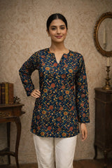 Woman wearing a floral patterned top in a room with a mirror and books.
