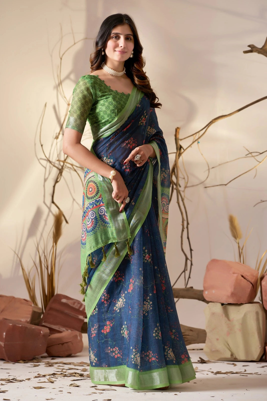 Woman wearing a green and blue saree with a decorative pattern, standing against a neutral background.
