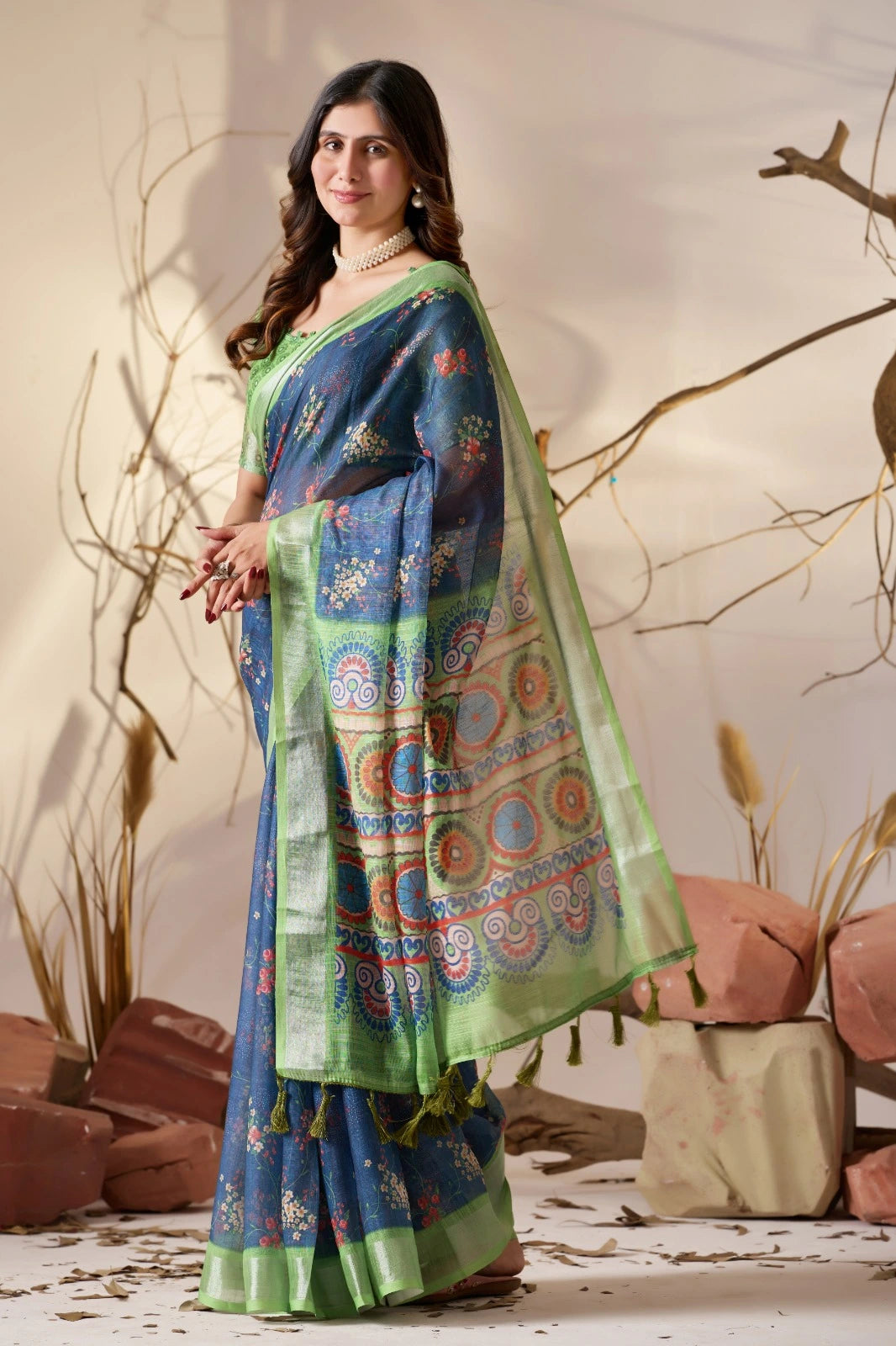 Woman wearing a blue and green saree with a patterned design, standing against a natural background.