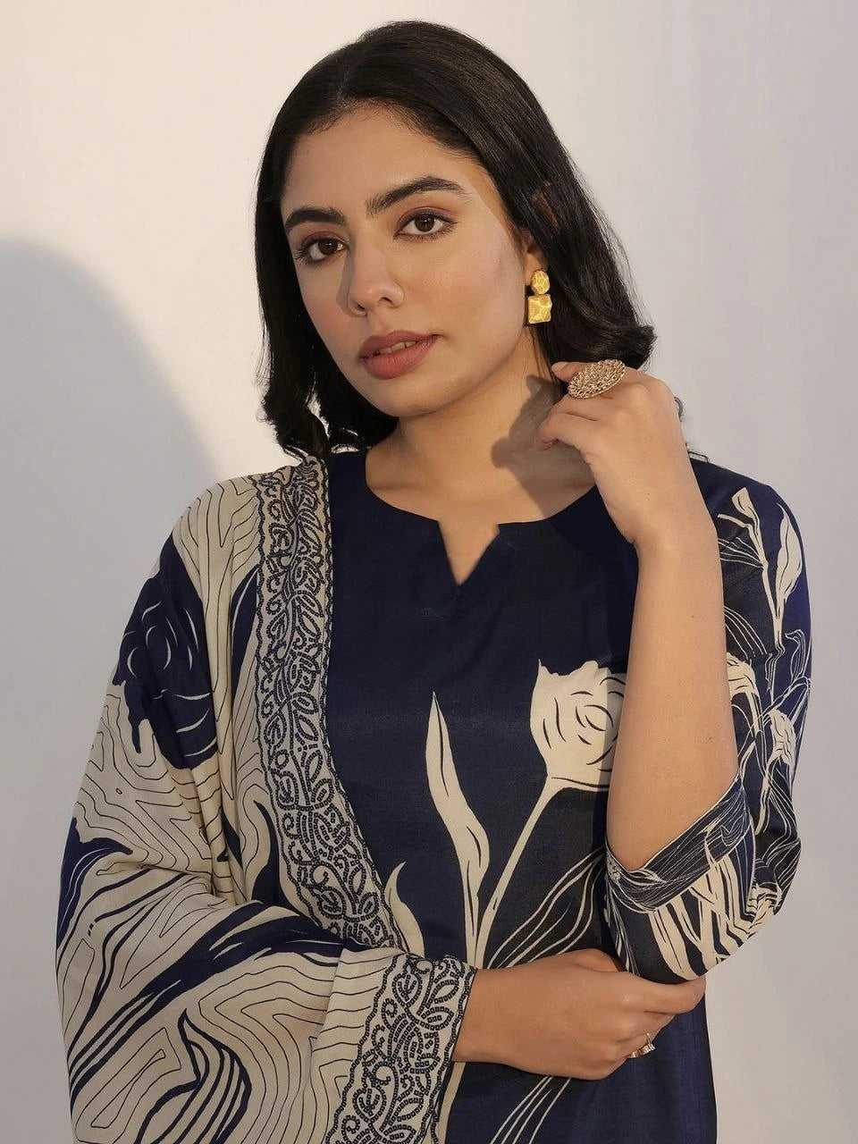 Woman wearing a navy blue and beige patterned outfit with gold earrings against a plain background
