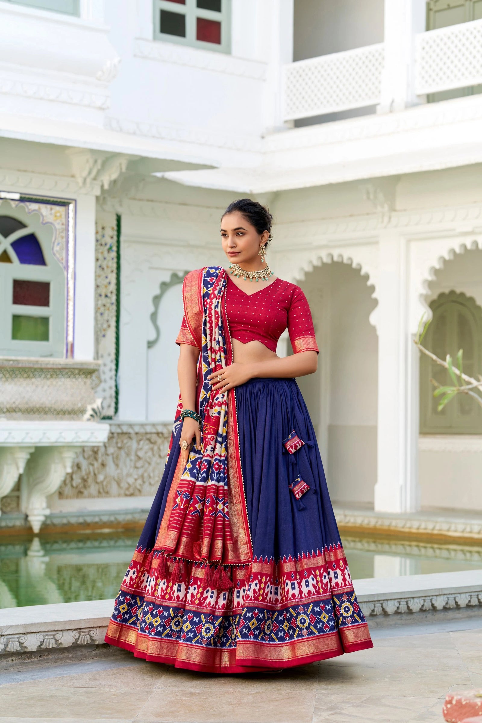 Woman in a traditional red and blue saree standing in an architectural setting.