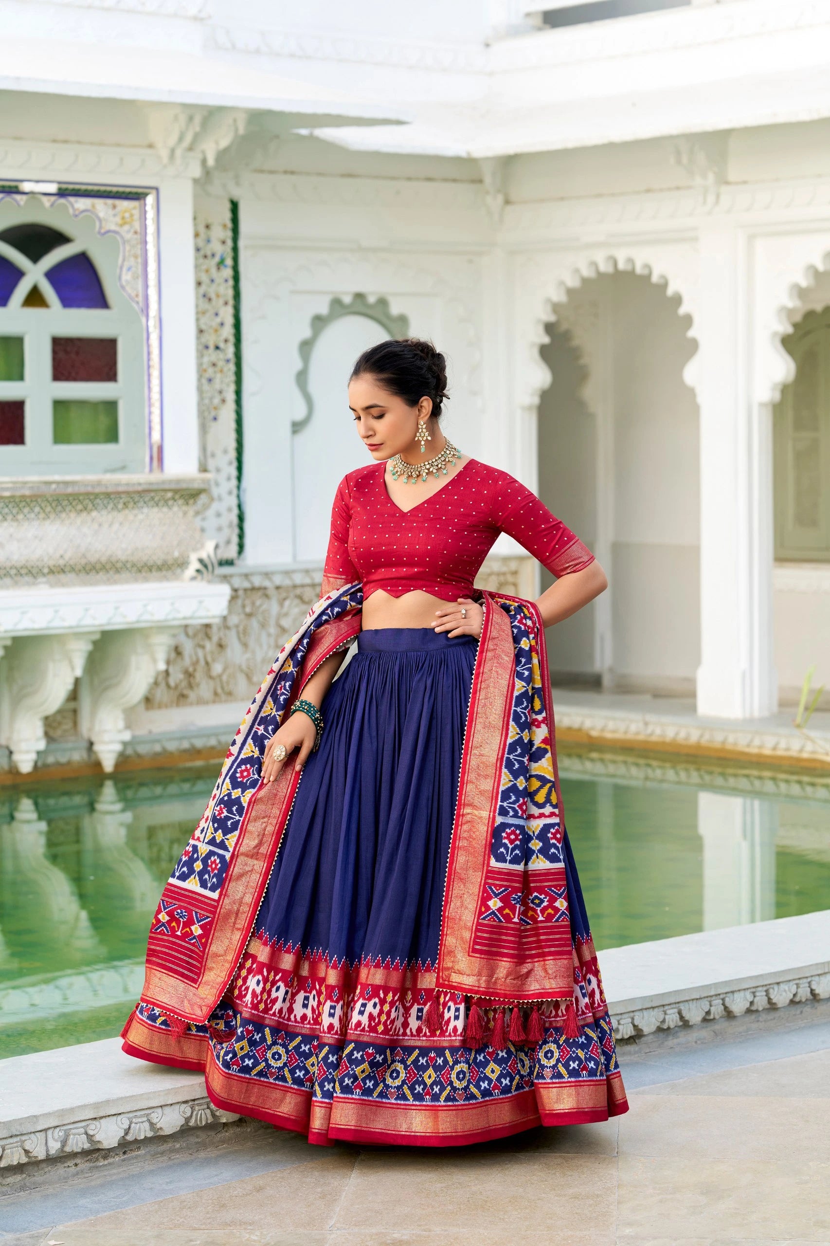 Woman in a red and blue traditional outfit standing in an elegant indoor setting.