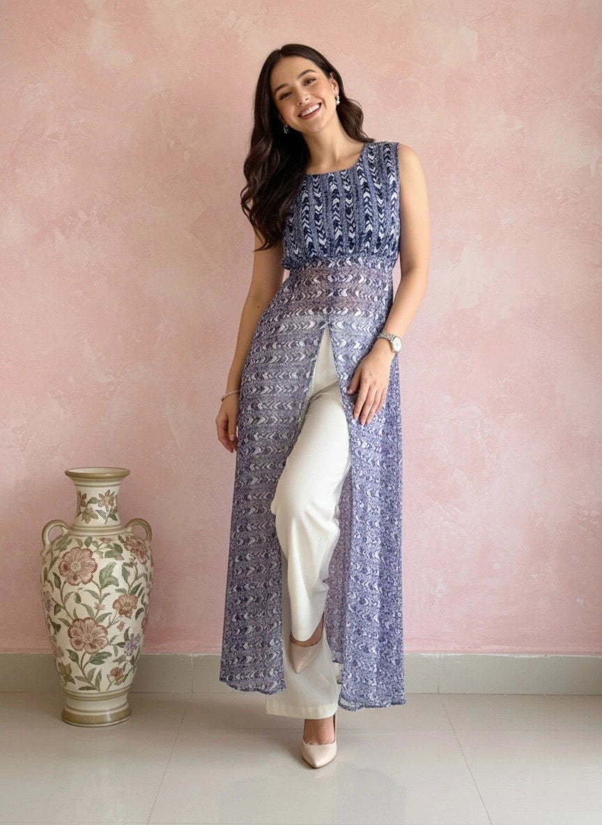 Woman wearing a blue patterned outfit standing next to a decorative vase against a pink wall.
