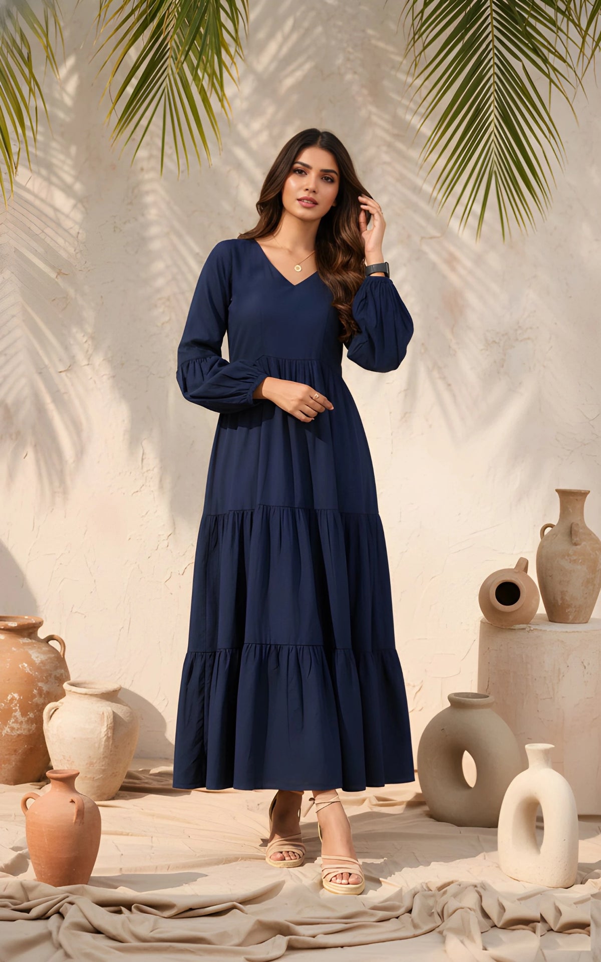 Woman in a navy blue dress standing in front of decorative vases and palm leaves.