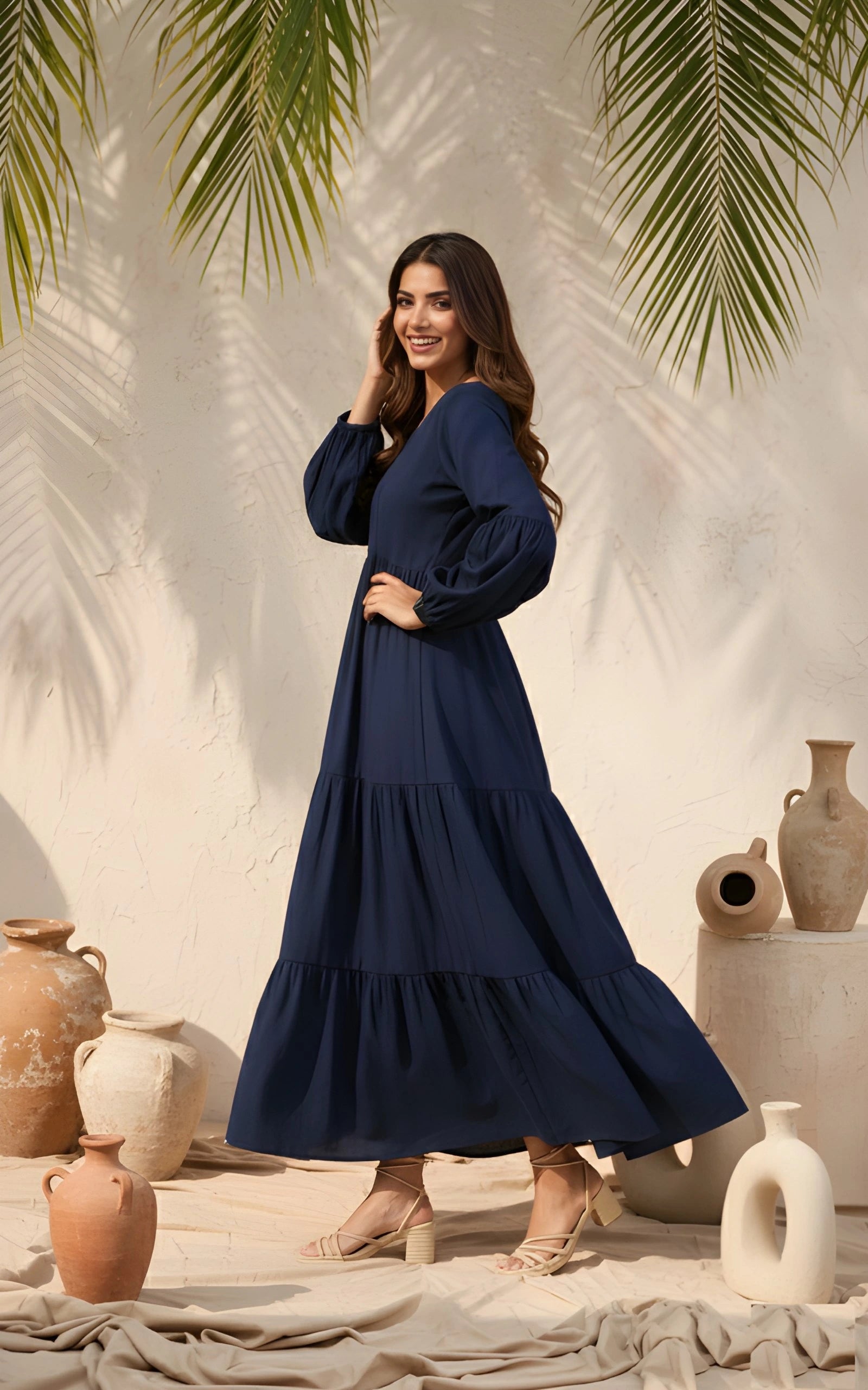 Woman in a navy blue dress standing in front of decorative vases and palm leaves.
