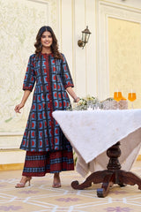 Woman in a patterned dress standing in a formal setting with a table and decor.