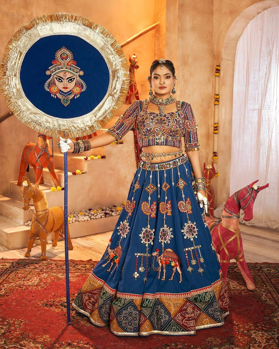 Woman in traditional embroidered outfit holding a decorative screen with a face design.